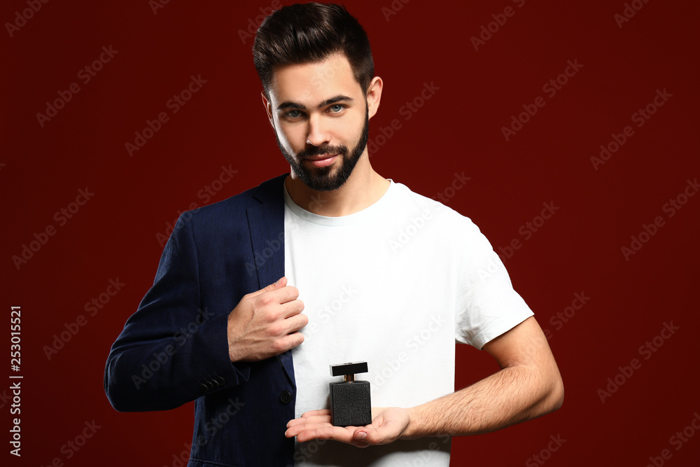 Handsome man with bottle of perfume on color background