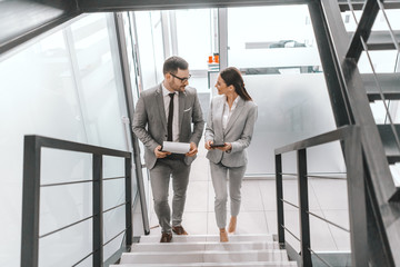 Two happy colleagues in formal wear climbing the staircase and talking. Teamwork is ability to work as a group toward a common vision.