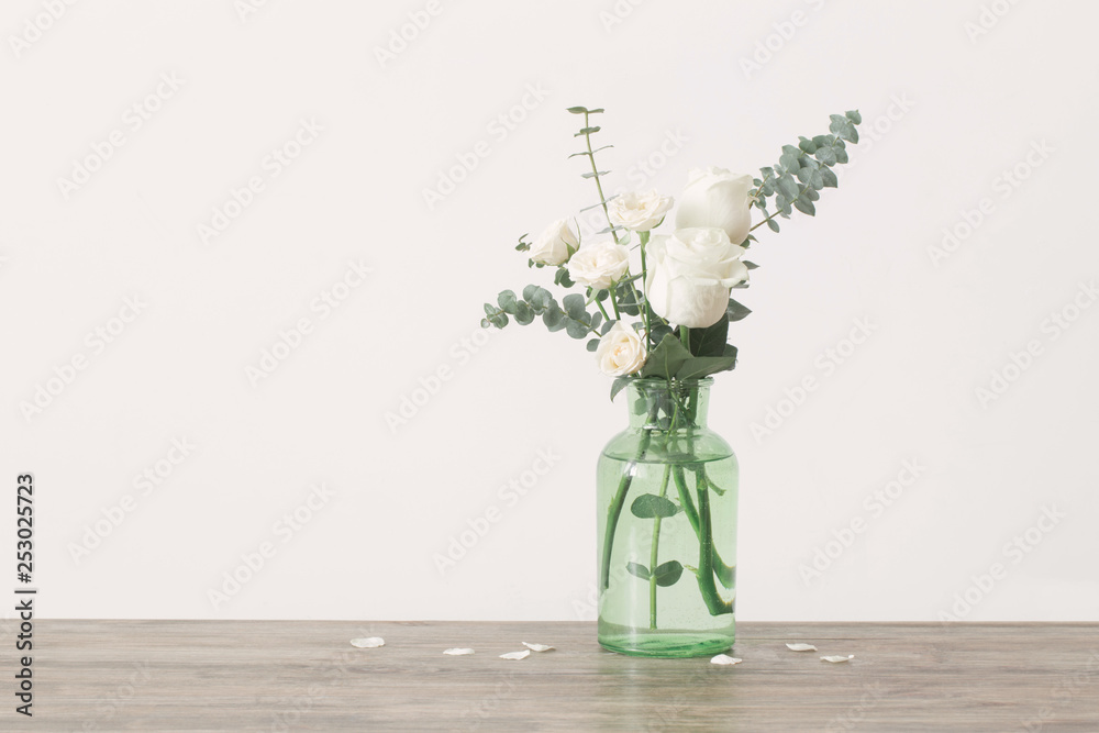 eucalyptus twigs and roses  in  glass vase on white background - obrazy, fototapety, plakaty 