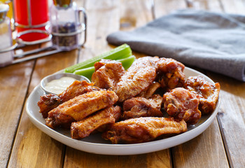 plate of bbq chicken wings with ranch dip and celery sticks on wooden table