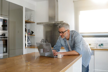 Wall Mural - Man with computer at home in modern kitchen