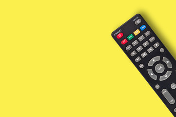 Single black plastic remote control for different multimedia devices on yellow background with copy space for your text. Top view