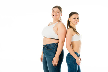 smiling slim and overweight women in denim posing together isolated on white, body positivity concept