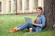 © Viktoriia - Young student at university campus sitting under the tree browsing web on laptop looking camera happy