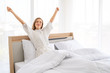 © paulfourk - Beautiful young smiling woman sitting on bed and stretching in the morning at bedroom