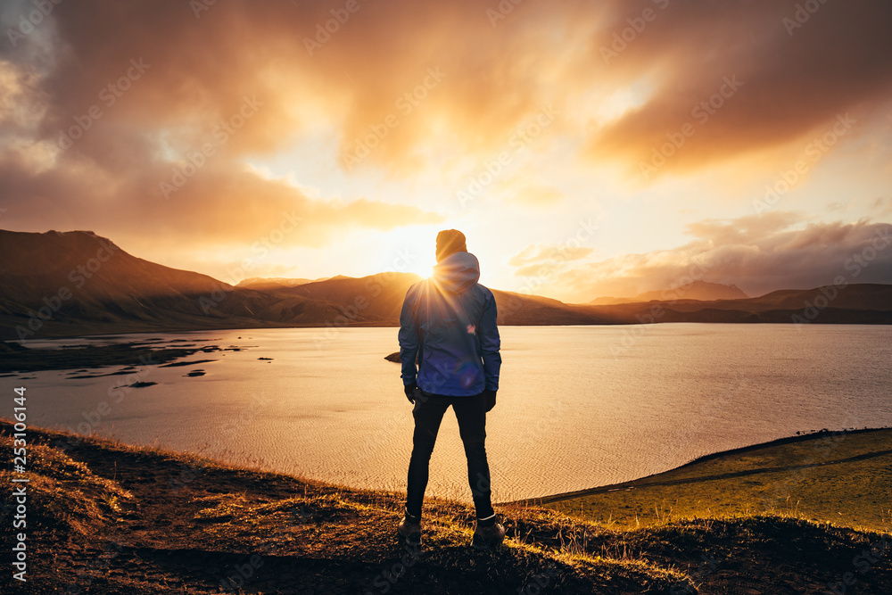 Man standing in blue jacket looking at spectacular sunset over frostadavatn lake in Landmannalaugar in Iceland - obrazy, fototapety, plakaty 