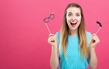 Wall Mural - Young woman holding paper glasses and mustache party sticks on a pink background