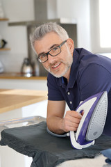 Poster - Mature man leaning on ironing board holding iron in modern kitchen