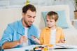 © LIGHTFIELD STUDIOS - smiling father and preschooler son holding paintbrushes and drawing at home