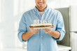 © LIGHTFIELD STUDIOS - cropped view of smiling man holding birthday cake with burning candles at home in morning