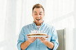 © LIGHTFIELD STUDIOS - excited handsome man holding birthday cake with burning candles at home in morning