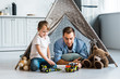 © LIGHTFIELD STUDIOS - father and preschooler son playing with toy cars and teddy bears under wigwam at home