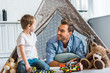 © LIGHTFIELD STUDIOS - smiling father and preschooler son playing with toy cars and teddy bears under wigwam at home