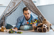 © LIGHTFIELD STUDIOS - adult man lying in wigwam and playing with toys in nursery