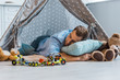 © LIGHTFIELD STUDIOS - adult man sleeping on pillow in wigwam with toys around