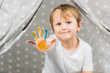 © LIGHTFIELD STUDIOS - cute preschooler boy with colorful paint on hand looking at camera at home
