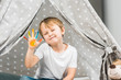 © LIGHTFIELD STUDIOS - adorable preschooler boy with colorful paint on hand sitting in wigwam at home