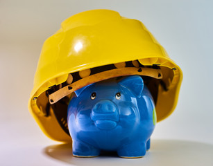 Blue piggy bank wearing a yellow construction helmet displaying saving for housing or house and expences for craftsmen