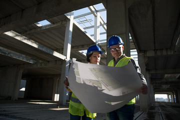 Male and female architects or business partners looking at floor plans on a construction site