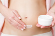 © fotoduets - Young woman's hands holding opened white cream jar and applying naked belly. Care about perfect, soft and smooth skin in pregnancy time. Closeup. Front view.