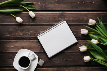 Wall Mural - White tulips on a wooden table with a Cup of coffee and an empty notebook