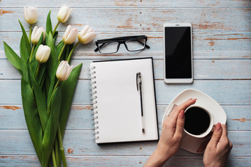 Wall Mural - Spring blanks freelance workplace with a bouquet of white tulips, smartphone and a Cup of coffee in his hands on a blue wooden background