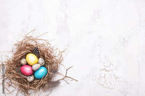 Colorful Easter eggs in nest on white craquelure background. Top view, copy s...