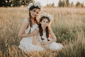 Happy mom and daughter smiling and hugging on the grass in the field in the summer