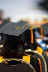 Rear view selective focus of the university graduates crowded in the graduation ceremony. The graduates stand in-line while waiting for  awarding degree certificate. Graduation congratulations