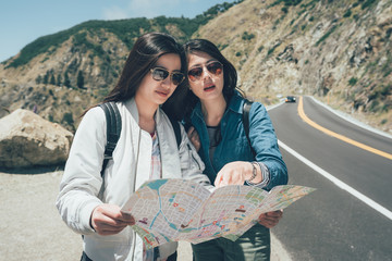 adventure travel tourism hike people concept. vintage photo group of smiling friends with backpacks and map outdoors standing on highway road trip in 17 mile drive california. girls talking on guide