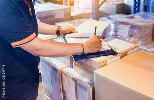 Cuadros en Lienzo Warehouse worker writing on clipboard with checklist details shipments boxes, Warehouse inventory managemant