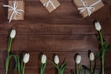 Fototapeta Tulipany - Row of white tulips and gift boxes on brown wooden table. Women day concept. White ribbon, craft wrap, 8 march, spring