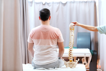 Man sitting on hospital bed with backs turned. Next to him doctor holding model of spine.