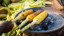 Sweet Corn Cob Roasting On A Coal And Unrecognizable Street Vendor Turning It. Indian Street Food Concept, Closeup.