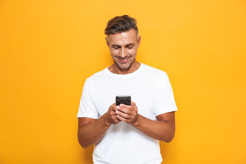 Happy man posing isolated over yellow wall background using mobile phone.