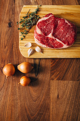 Overhead shot of ribeye steak resting on a wooden board in the kitchen with fresh thyme, onions and garlic cloves. Top shot