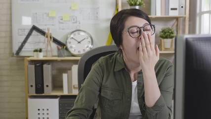 Wall Mural - slow movement of focus face on girl interior designer worker sitting at desk using computer working in office feeling tired yawning. bored exhausted woman architect overworked lack of sleep concept.