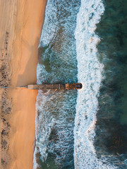 Wall Mural - Top down aerial view of wave coming into beach shore with stormwater pipe.