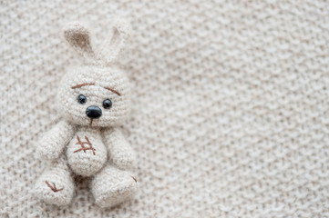 Knitted white hare is lying on a light knitted handmade fabric. There is a free space.