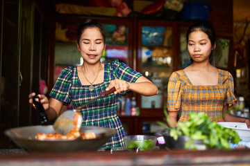 Wall Mural - thai mother and daughter cooking red curry together in tradional home kitchen