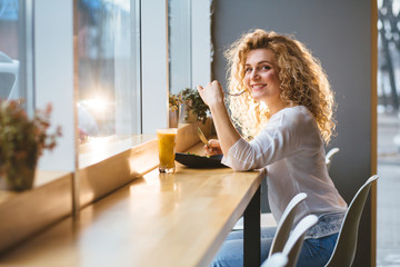 Wall Mural - Charming curly blond woman with beautiful smile eating salad during rest in coffee shop, happy Caucasian female have a dinner while relaxing in cafe during free time.