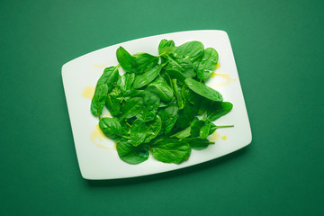 Baby spinach in a white plate on a green table.