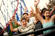 Smiling Family Riding On A Rollercoaster At An Amusement Park.