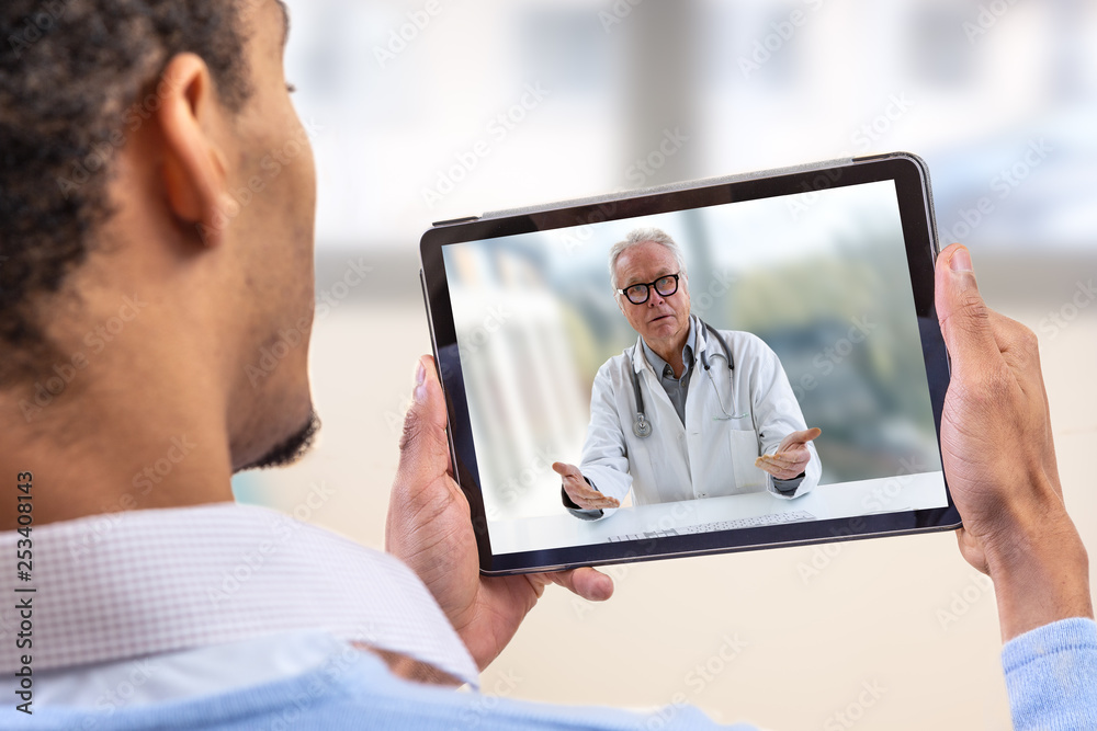 virtual live chat with the patient with digital tablet and a doctor via internet. In-home care for a young male patient in telemedicine or telehealth, - obrazy, fototapety, plakaty 