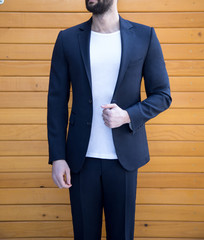 Wall Mural - Man in expensive custom tailored suit standing and posing outdoors infront of wooden background