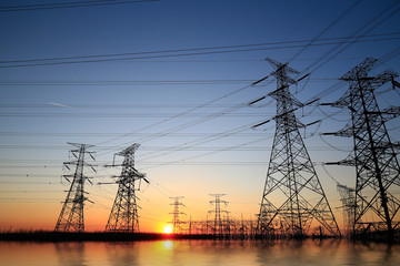 A high-voltage tower in the setting sun against the sky