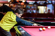 © Natali - Cute boy in yellow t shirt plays billiard or pool in club. Young Kid learns to play snooker. Boy with billiard cue strikes the ball on table. Active Leisure, sport, hobby concept