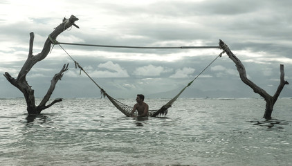 Wall Mural - man lying relaxed and happy in sea hammock amazing set up on tree trunks at tropical island beach in relaxing holidays travel getaway and tourist destination