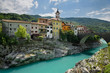 Colorful stucco houses on the turquoise Soca River with stone bridge at old section of Kanal Slovenia with Assumption of Mary church