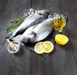 Wall Mural - Dorado fish on black boards with lemon and spices. Fresh sea fish with olive oil, spices and lemon ready for cooking. Raw fish cooking and ingredients. Dorado, herbs and spices. 